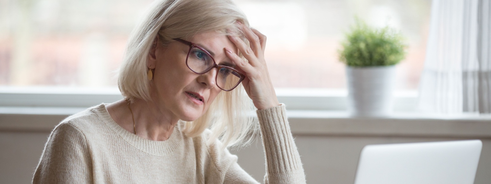 A retired woman looking worried while using a laptop.