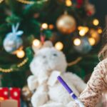 A girl writing a letter in front of a Christmas tree.