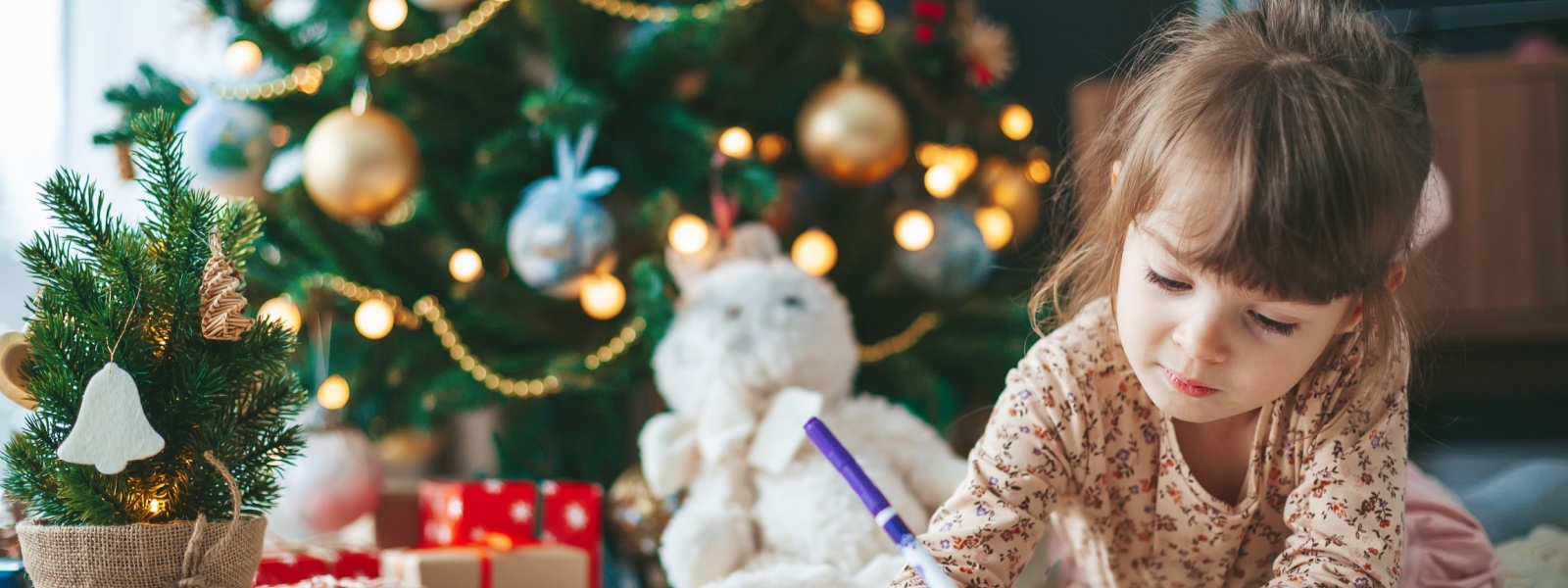 A girl writing a letter in front of a Christmas tree.