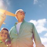 A grandfather and grandson playing with a toy plane outdoors.