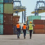 Workers walking through a shipping cargo container terminal depot.