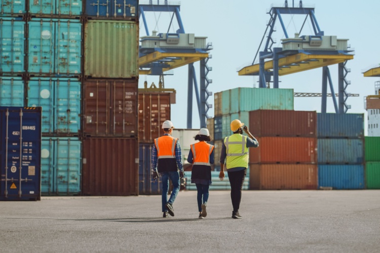Workers walking through a shipping cargo container terminal depot.