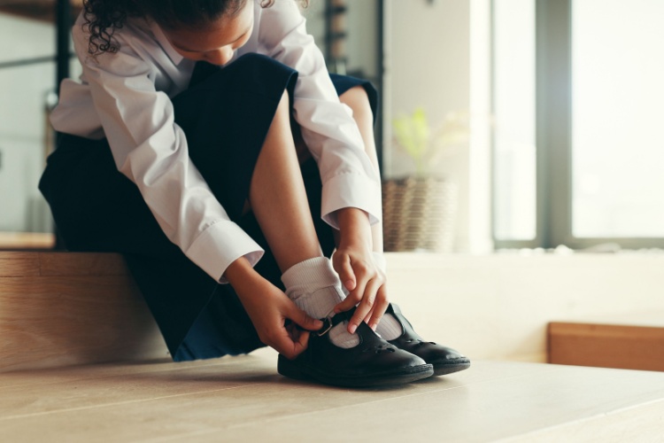 A girl putting on school shoes.