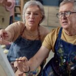 An older couple painting at an easel together.