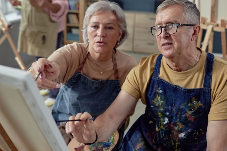 An older couple painting at an easel together.