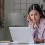 A woman at her computer, thinking carefully.