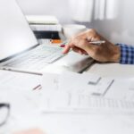Man’s hands at a laptop, with financial paperwork