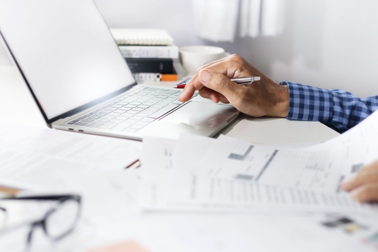 Man’s hands at a laptop, with financial paperwork