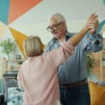 Two happy pensioners dancing at home, holding hands and having fun