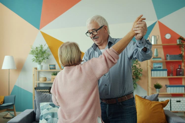 Two happy pensioners dancing at home, holding hands and having fun